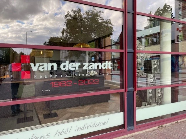 Etalage van Van der Zandt Keukens met logo, tekst 'Keuken Interieur', jaartallen 1982-2022 en interieuritems