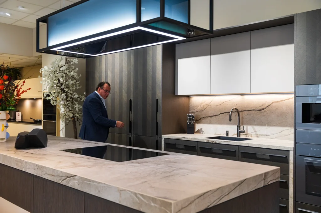 Moderne keuken met groot marmeren eiland, donkere kasten, lampen en man bij gestreepte koelkast