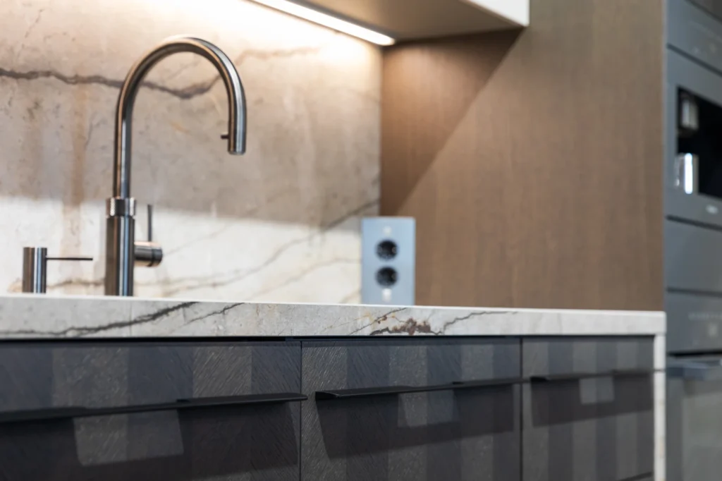 Moderne keuken met gebogen chromen keukenkraan, marmeren aanrechtblad en donkere kasten met handgrepen