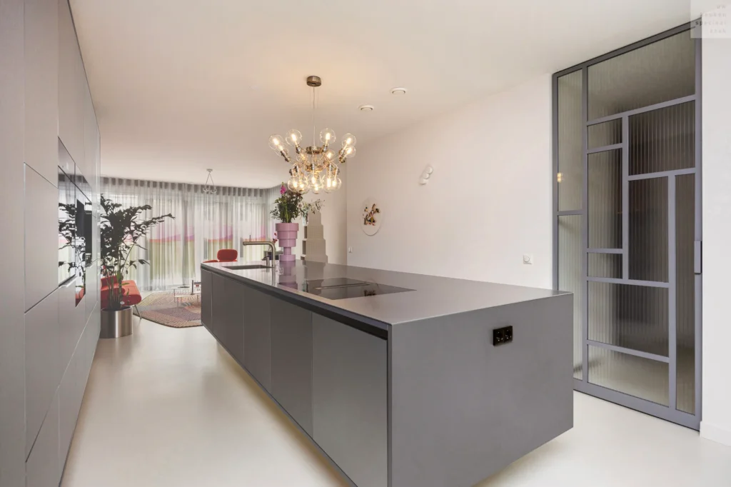 Strakke moderne keuken met greeploze grijze kasten en een roestvrijstalen werkblad in een lichte ruimte.