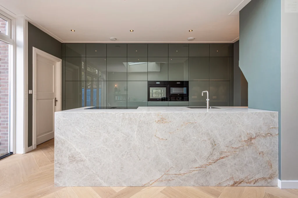 Moderne keuken met groot lichtmarmeren kookeiland, donkere kasten en visgraatvloer van hout