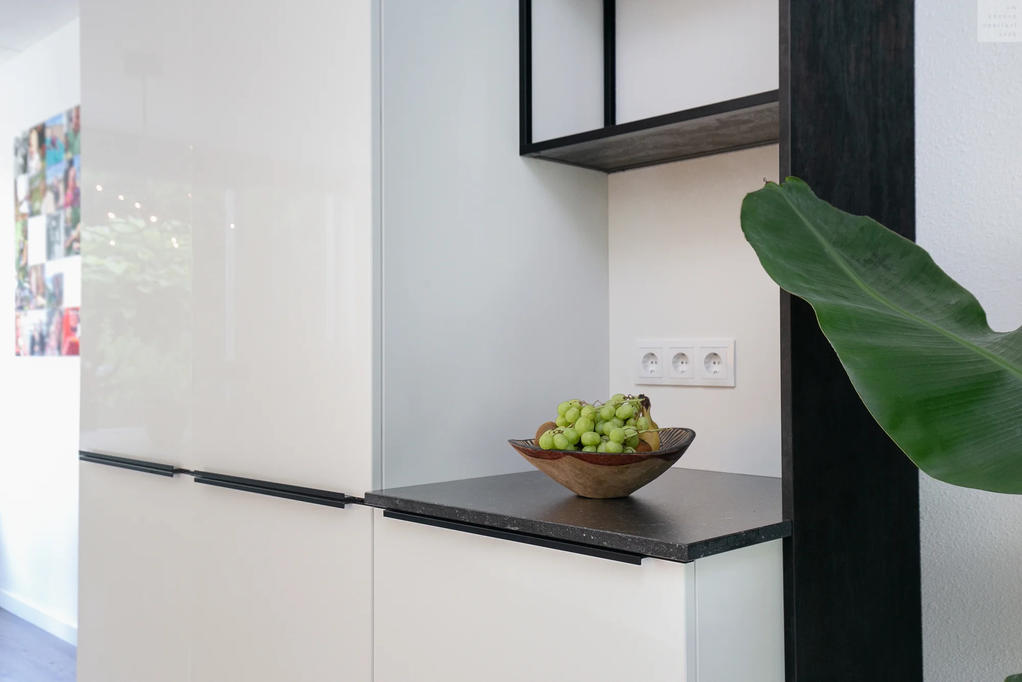 Moderne keuken met witte kast, zwarte handgrepen, houten schaal met druiven en open plank