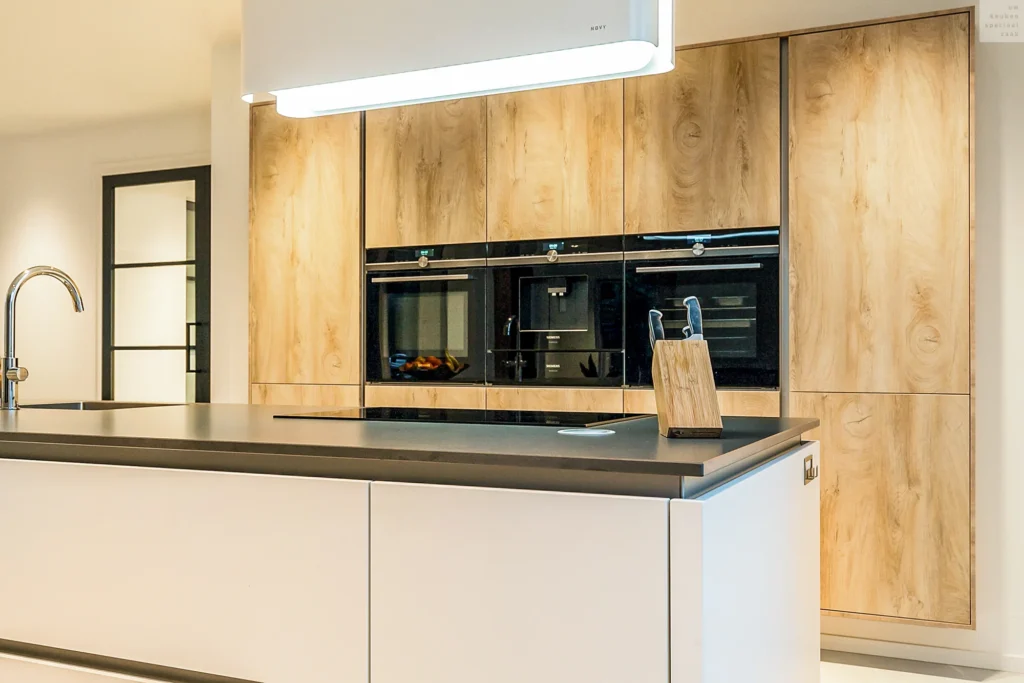 Moderne keuken met donker kookeiland, houten kasten en zwarte inbouwapparaten onder strakke lamp