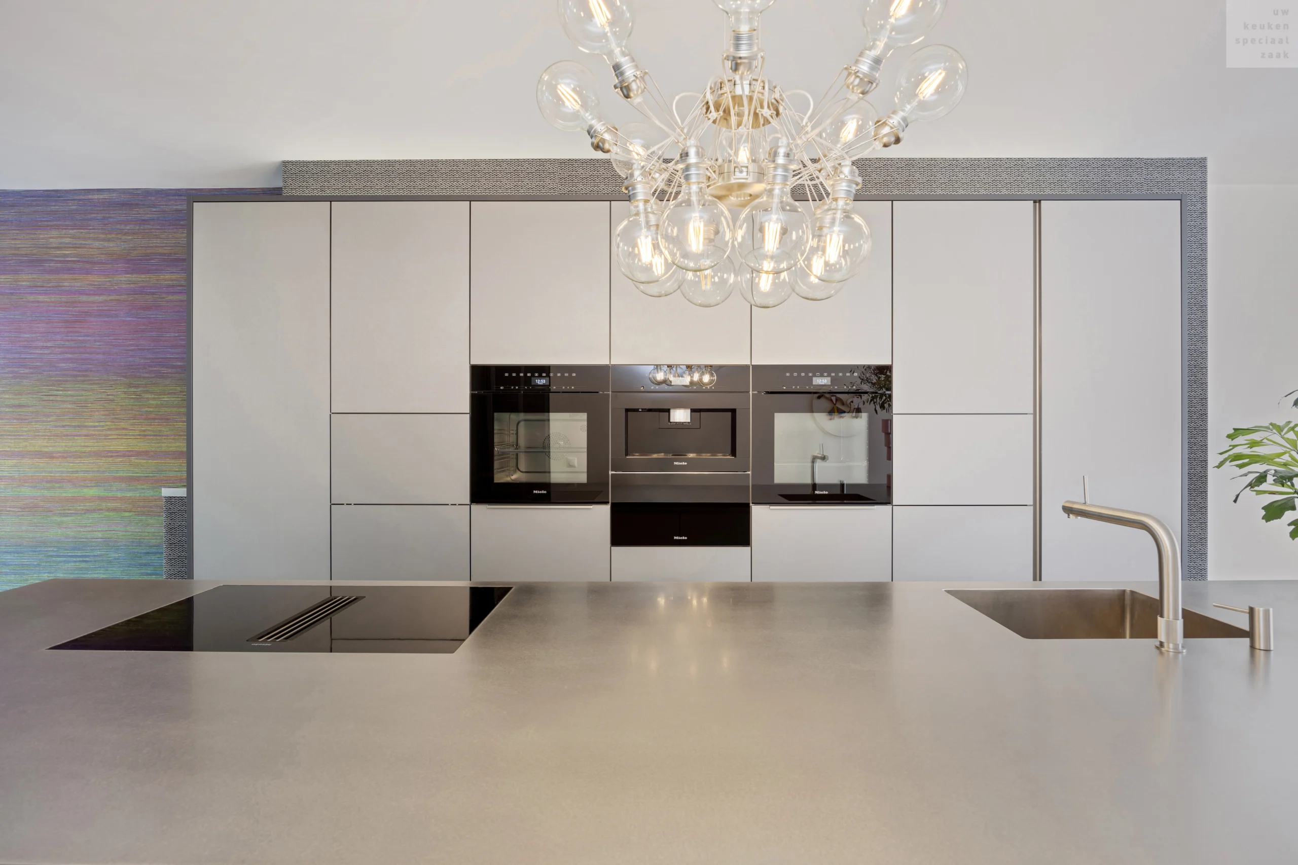 Moderne keuken met lichte kasten, zwarte inbouwoven, ronde lampen en glanzend metallic aanrechtblad