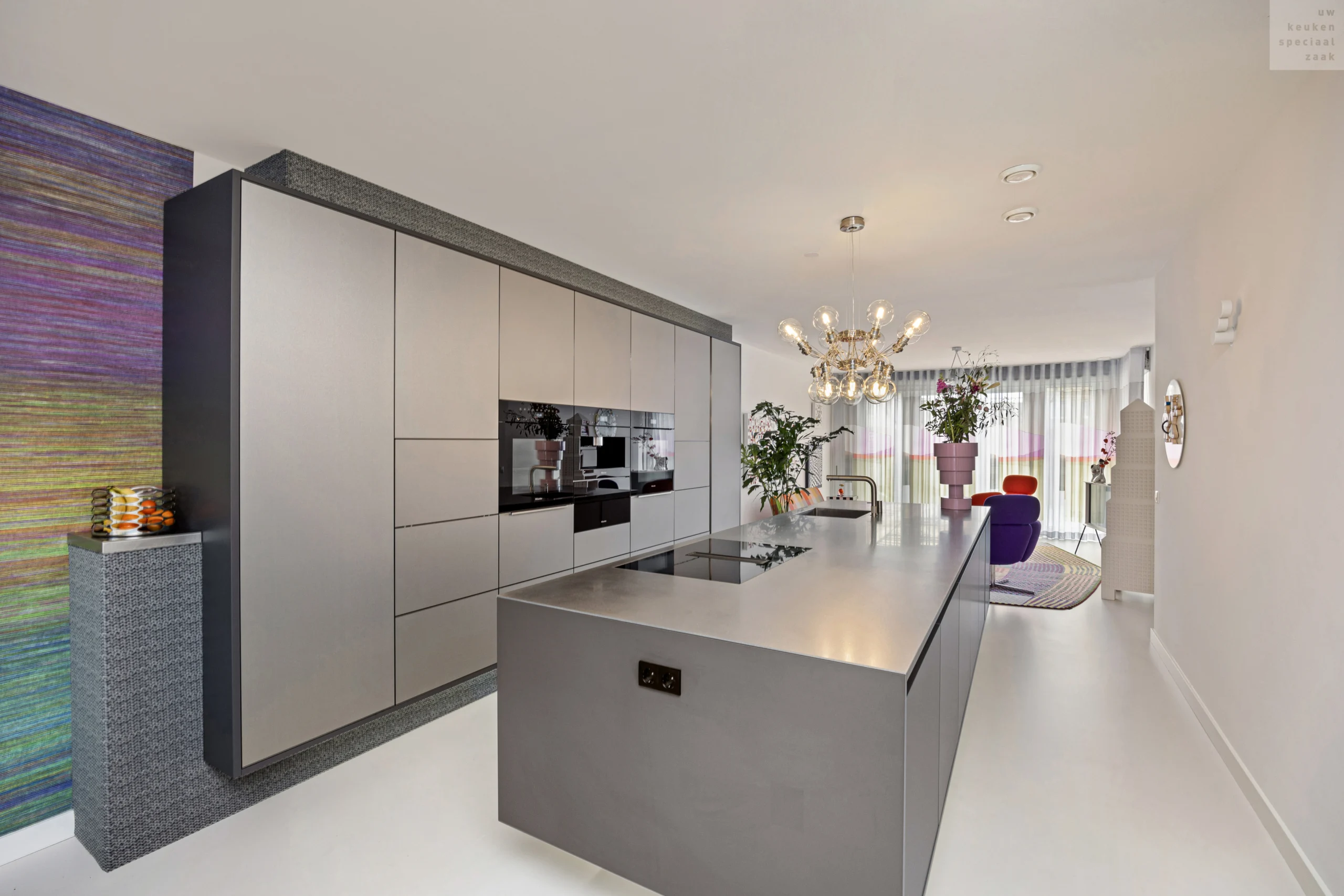 Moderne RVS keuken met zilverkleurige kastjes, kookeiland met glanzend blad en grote kroonluchter erboven