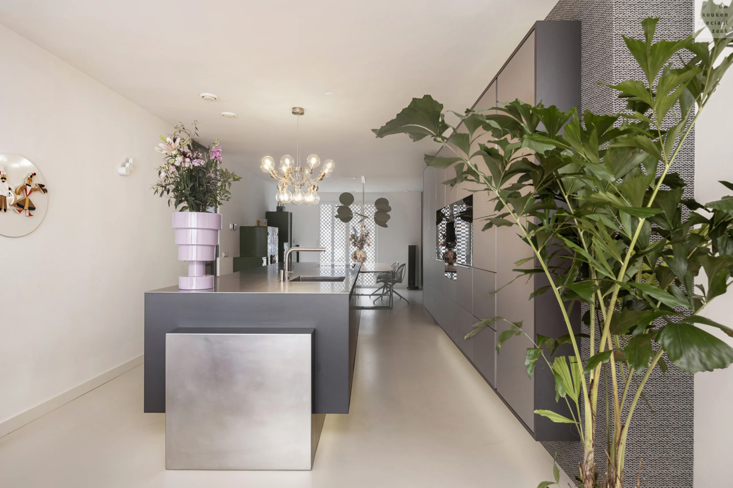 Moderne keuken met open indeling, grijze kasten, keukeneiland met metalen blad en paarsachtige bloempot