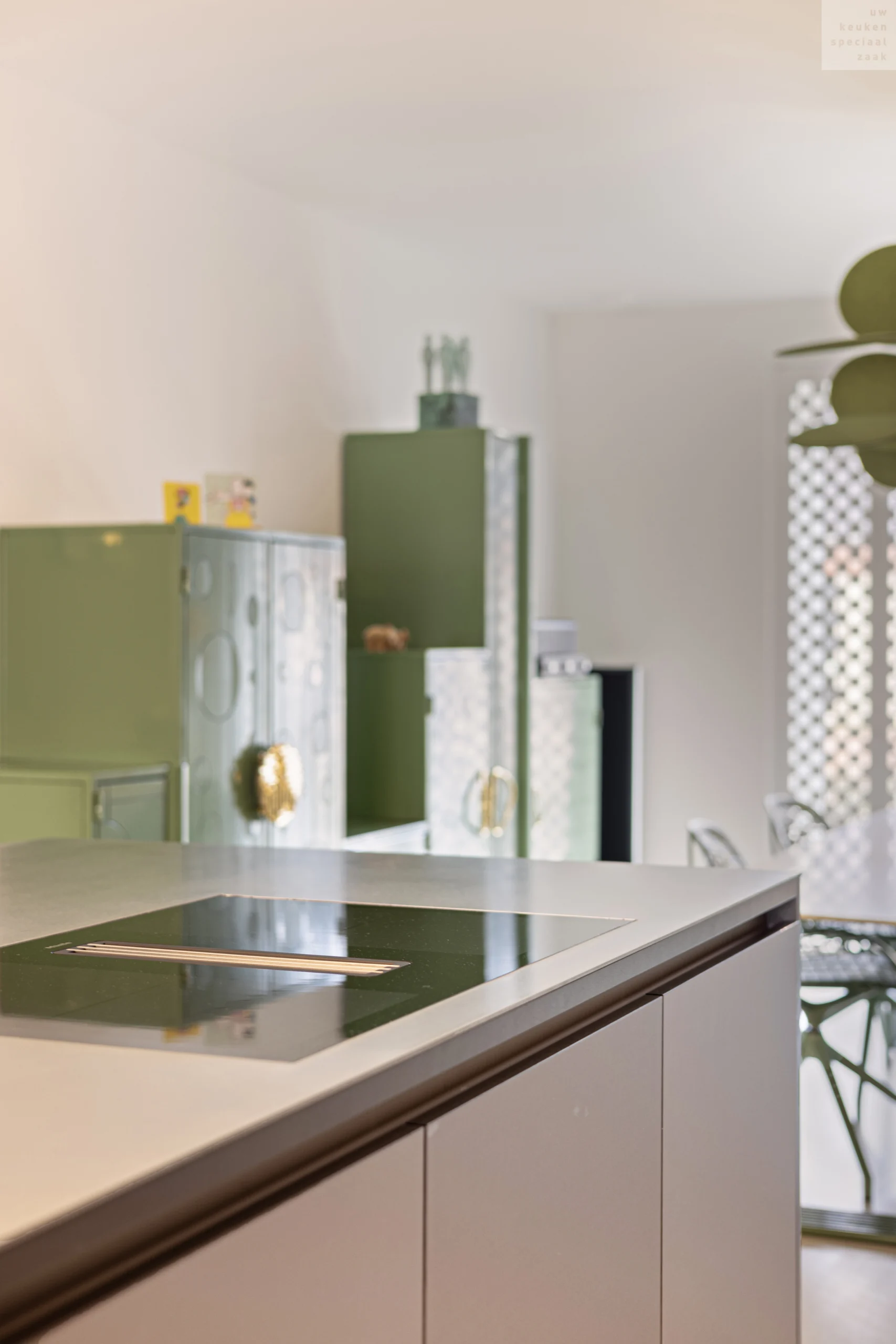 Moderne keuken met donkergrijs kookplaat, groene kastjes met glazen voorkant en lichtgekleurde stoelen