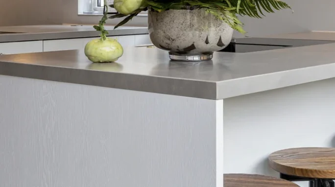 Modern licht keukenblok met ronde vaas gevuld met groene bladeren, groente en houten krukken