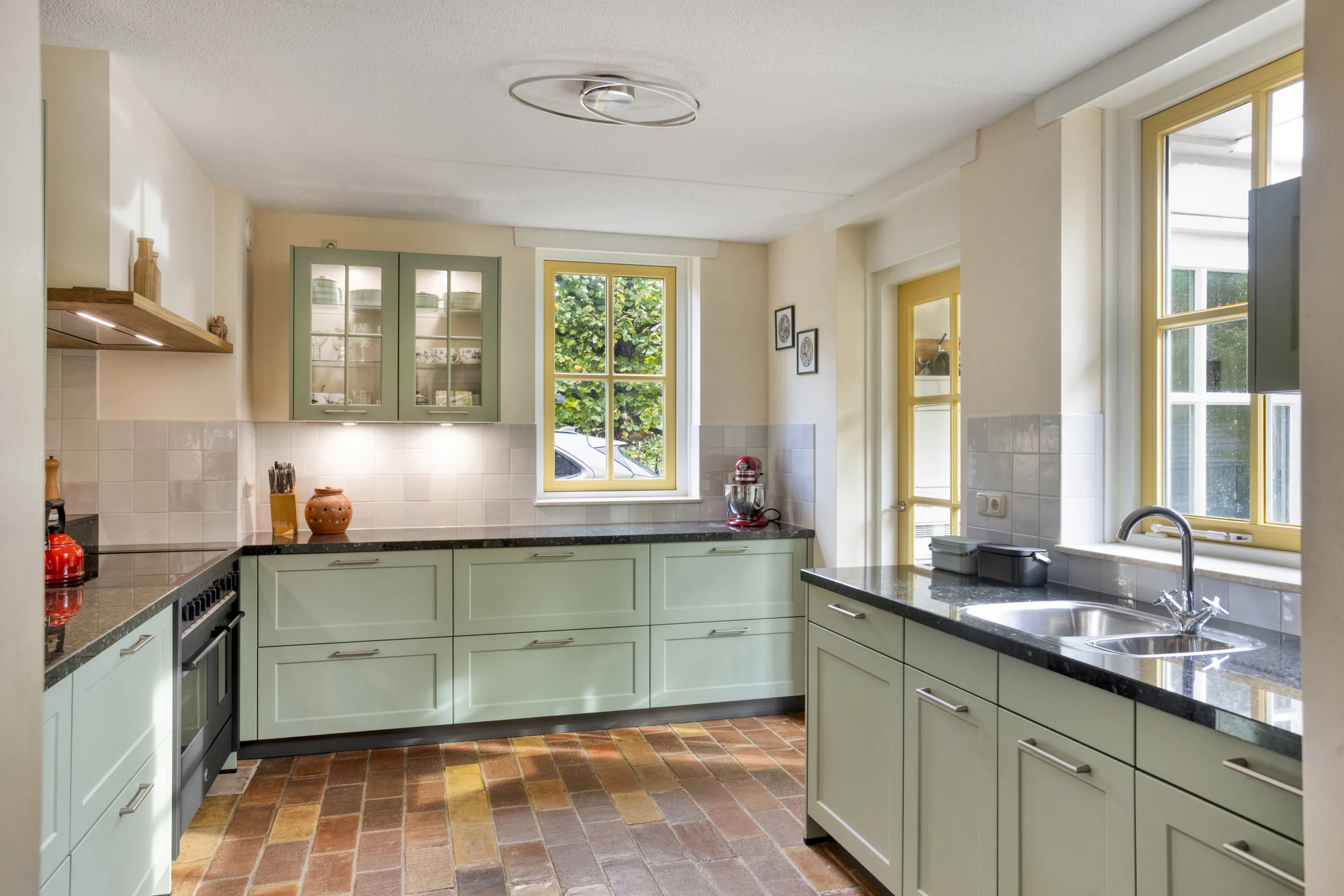 Moderne keuken met mintgroene kastjes, donker granieten aanrechtblad en glazen bovenkasten.