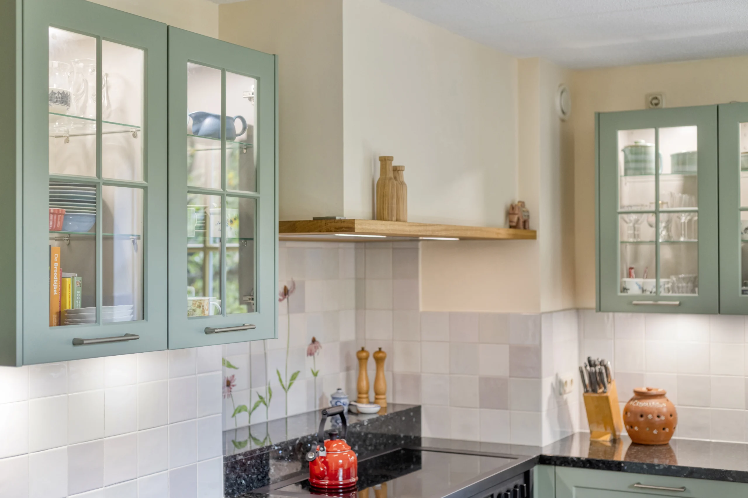 Moderne keuken met lichtgroene keukenkastjes met glas, witte tegels en rode waterkoker op zwart aanrecht