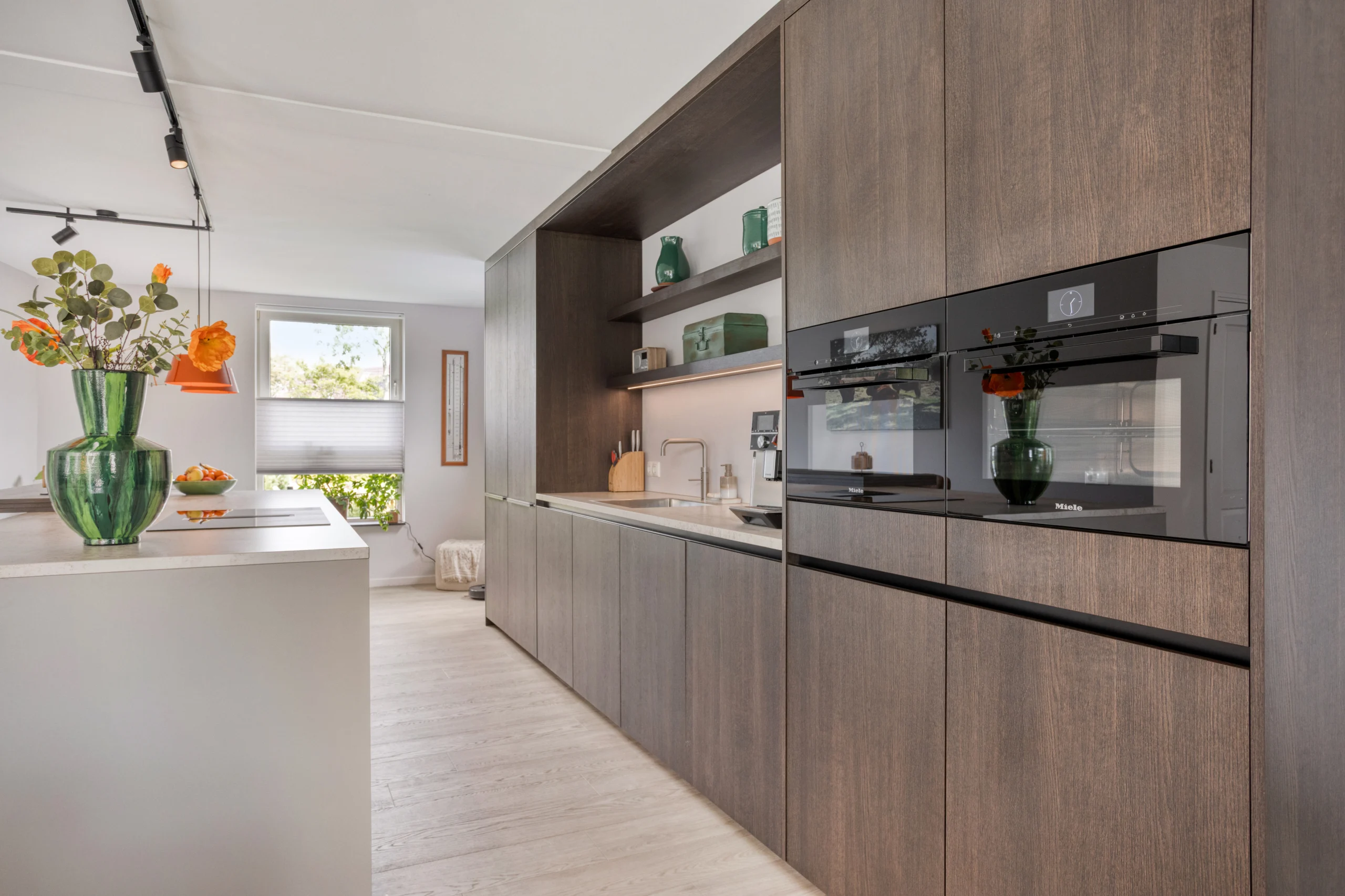 Moderne keuken met donkerbruine houten kasten, kookeiland, ingebouwde toestellen en open plank.