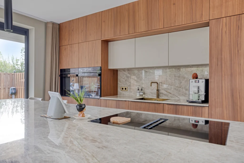 Moderne keuken met houten kasten, marmeren werkbladen, glazen kookplaat en gouden kraan naast een koffiezetapparaat