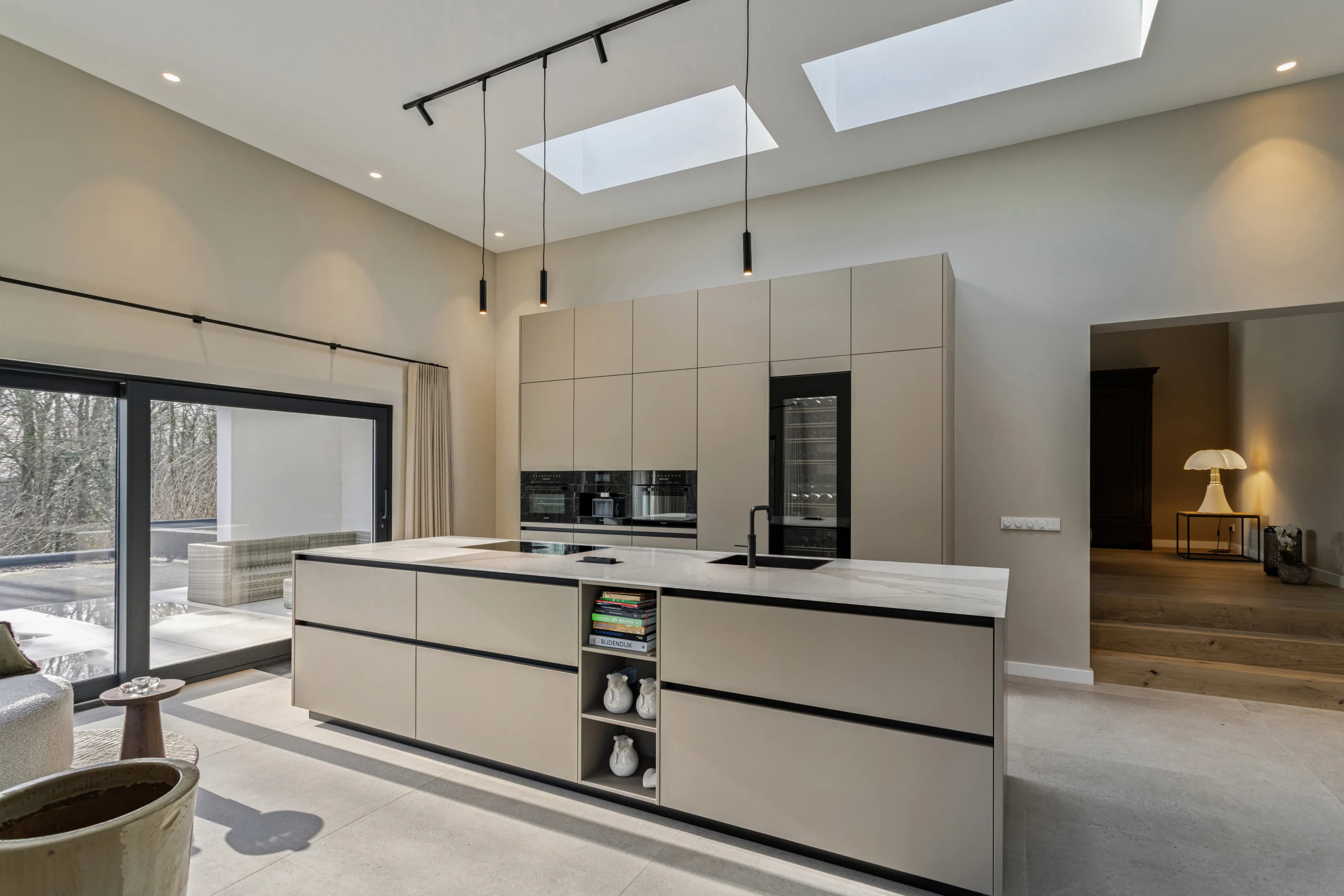 Moderne keuken met groot wit keukeneiland, donkere spoelbak, oven, wijnkoelkast en industriële lampen