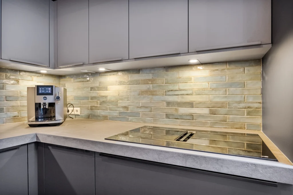 Moderne keuken met koffiemachine, groene en beige betegelde achterwand, lichtgrijs werkblad en keukenkastjes
