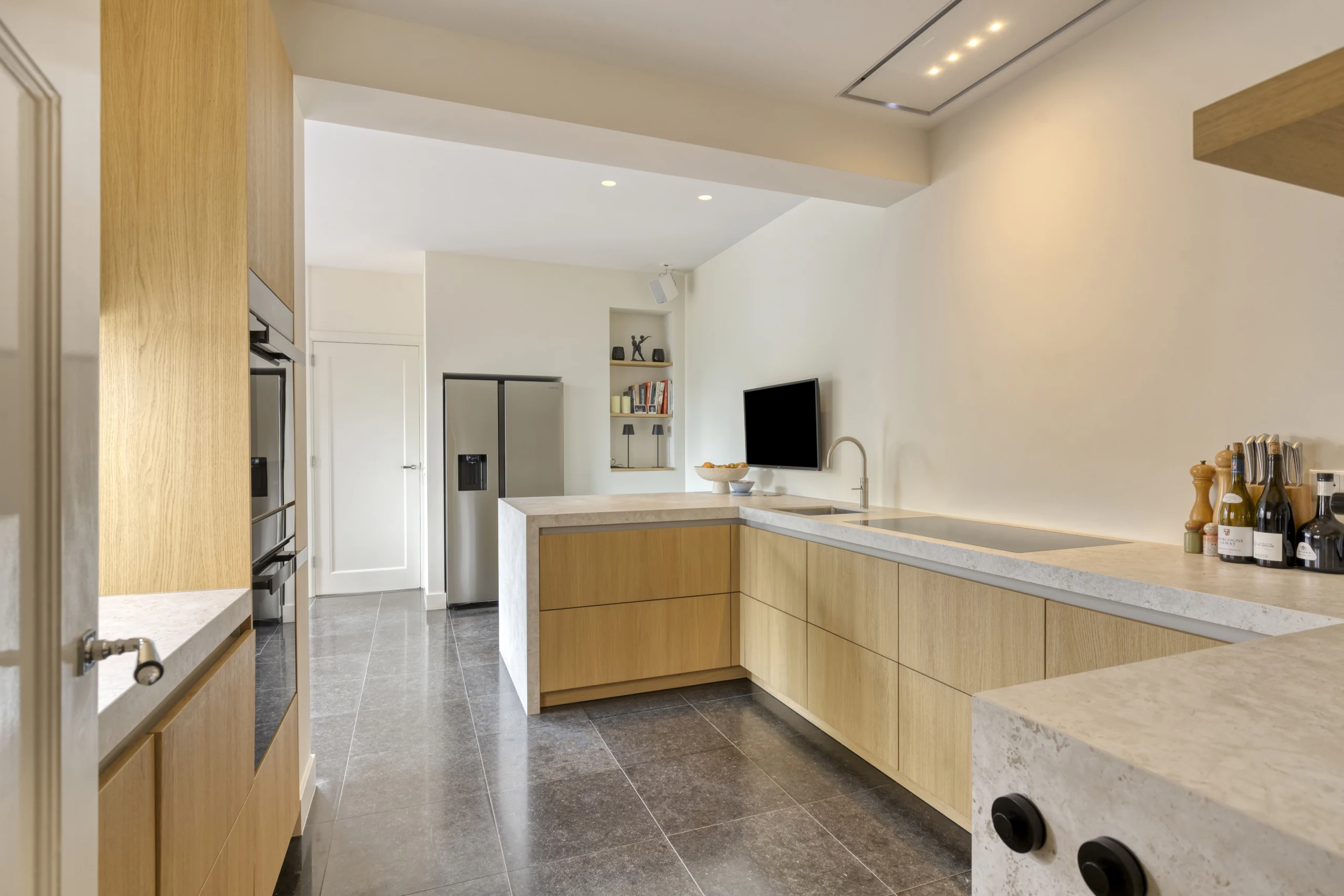 Moderne minimalistische keuken met lichte houten kasten, betonlook eiland en grote zilveren koelkast