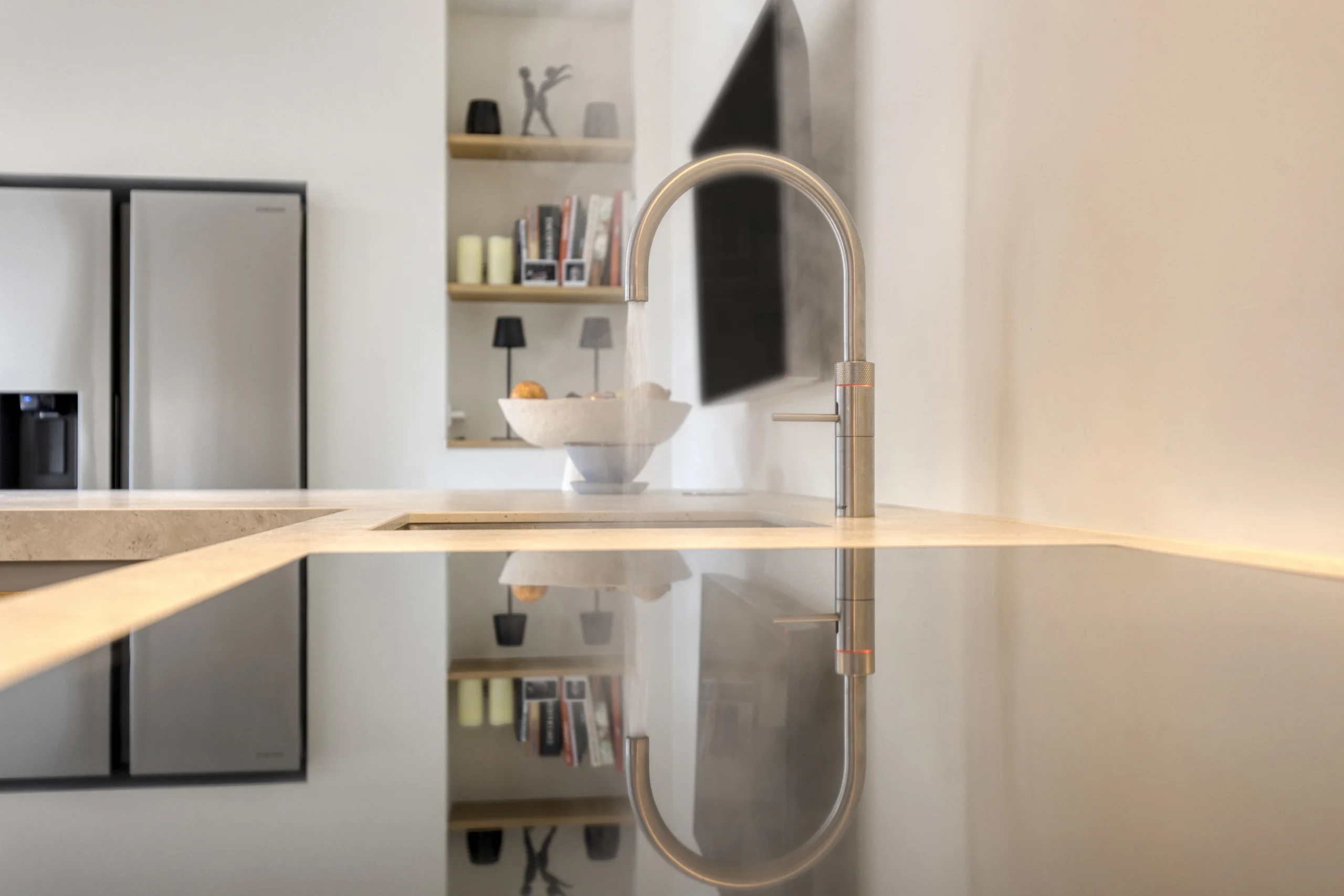 Moderne keuken met glanzend keukenblad, stalen kraan, zilverachtige koelkasten en open planken met fruit en boeken