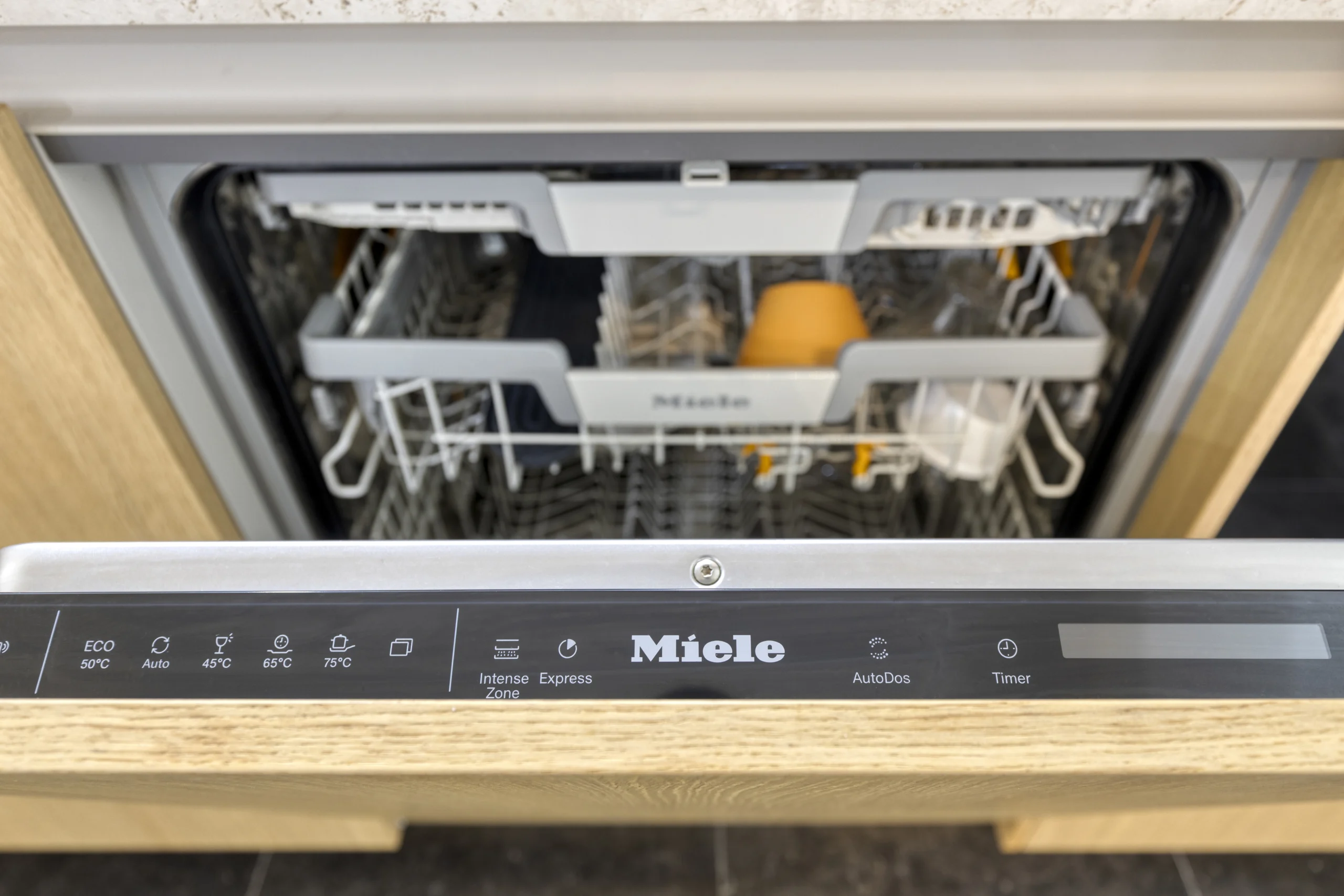 Open Miele vaatwasser met zichtbare rekken, controlepaneel en kleurrijk serviesgoed geplaatst