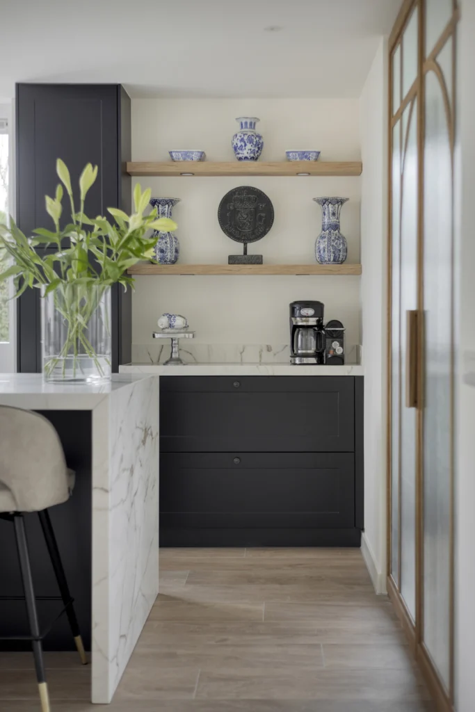 Moderne keuken met glazen deur, houten planken met vazen, donkere kasten en marmeren keukenbar met barkruk.