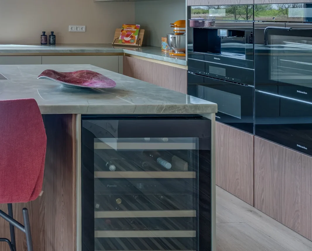 Moderne keuken met groen marmeren eiland, rode stoelen, glazen, wijnfles en groot raam uitzicht bomen
