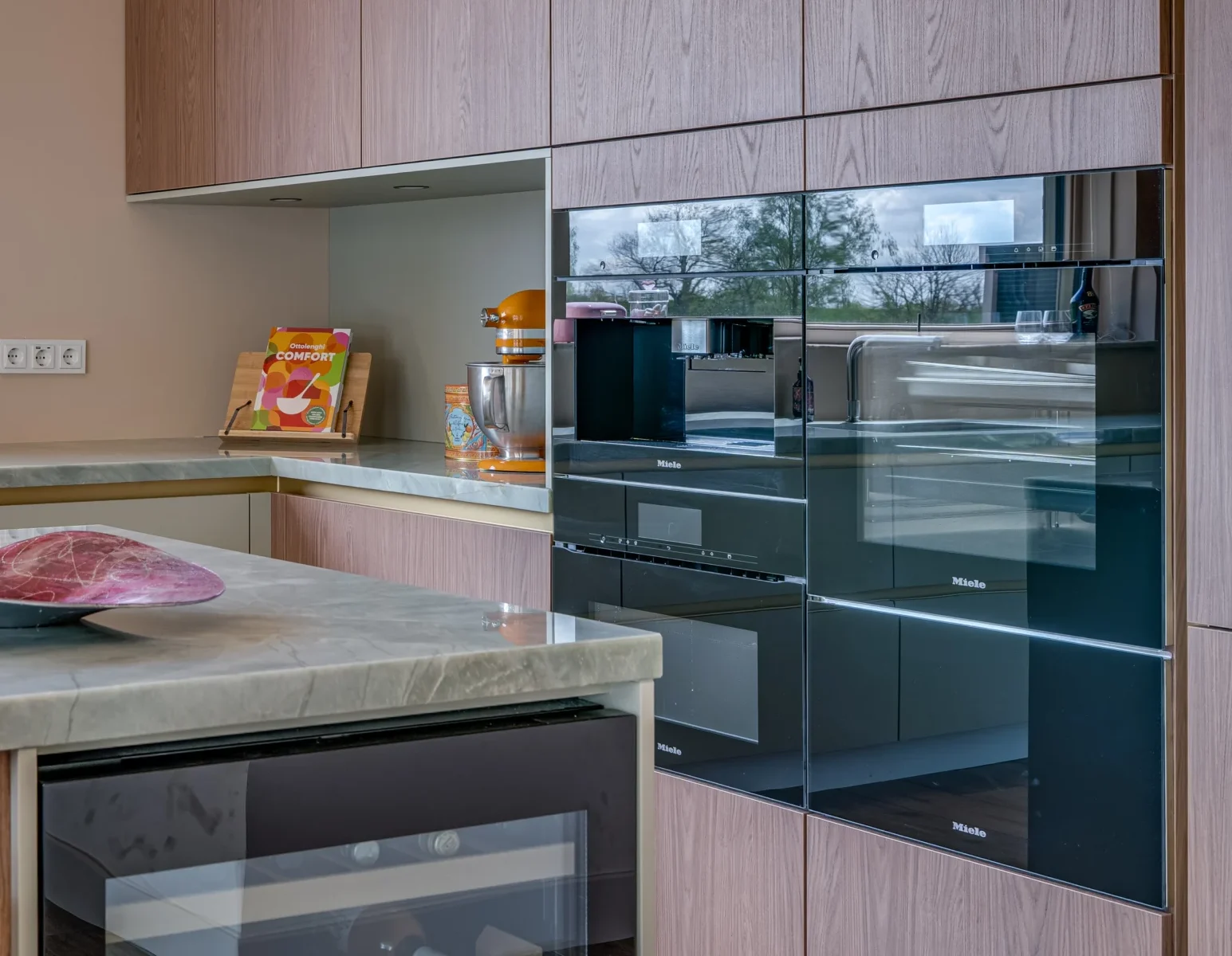 Moderne keuken met donkere houten kasten, licht marmeren aanrecht en diverse keukentoestellen.