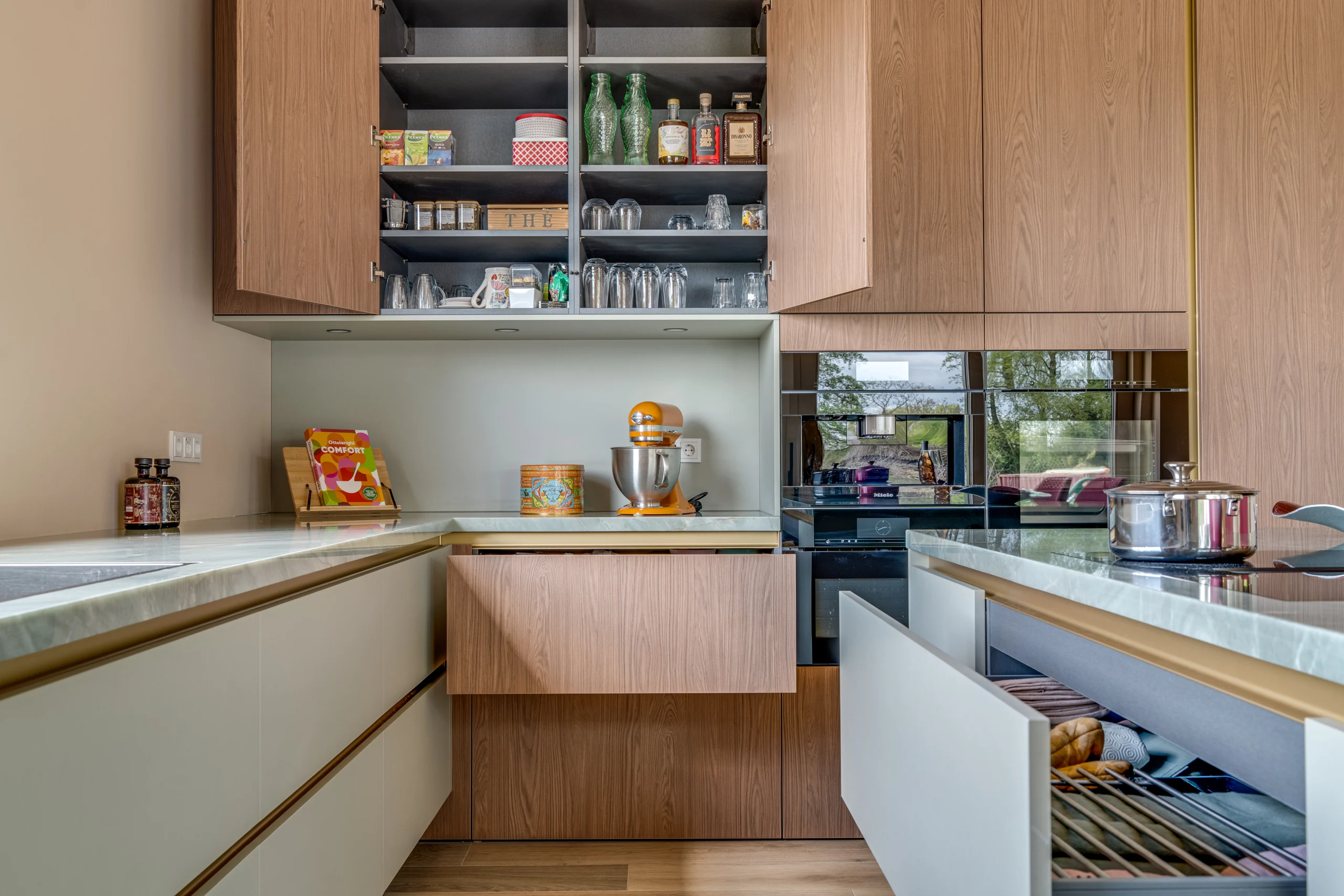Moderne keuken met houtkleurige en witte keukenkastjes, oranje keukenmachine en open lades met keukengerei