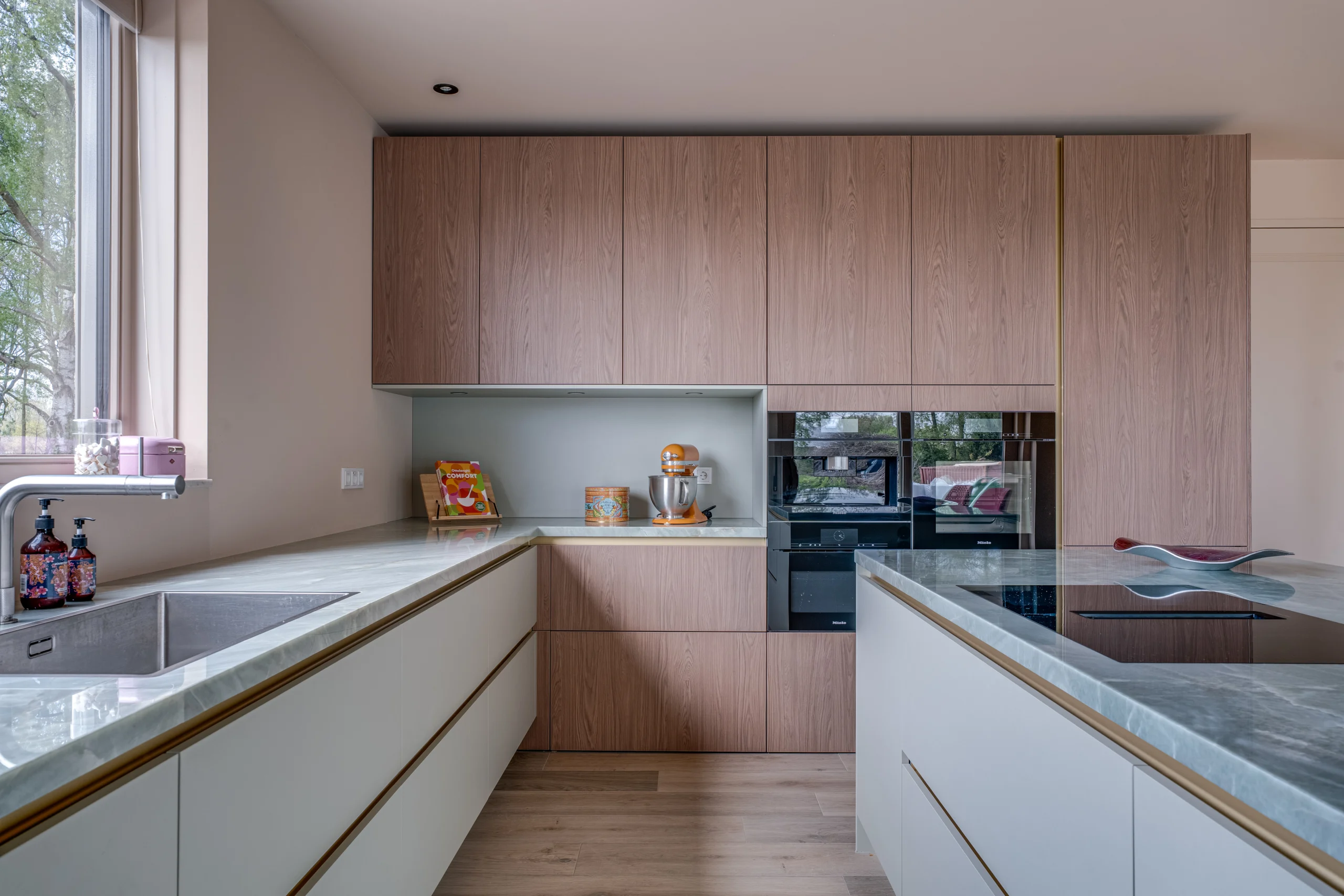Moderne keuken met lichtgekleurde en houten kasten, marmeren werkblad en grote ramen