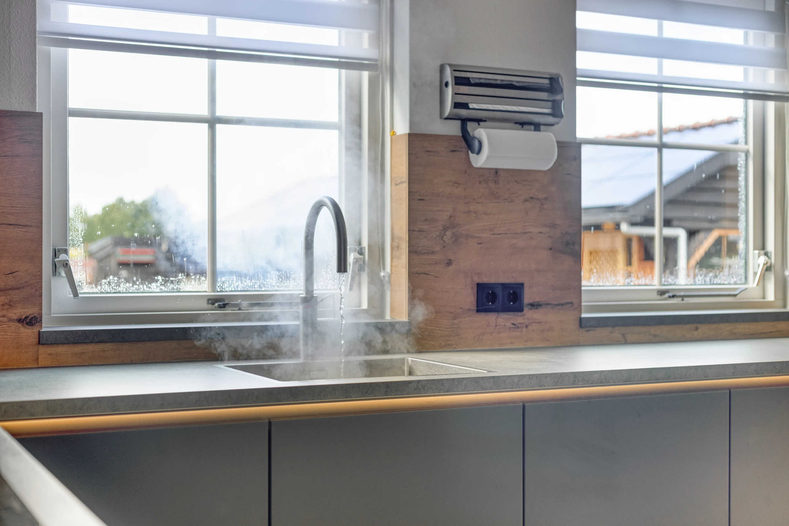 Moderne keuken met een grote gootsteen rechts, stromend water en stoom, houten achterwand en licht werkblad