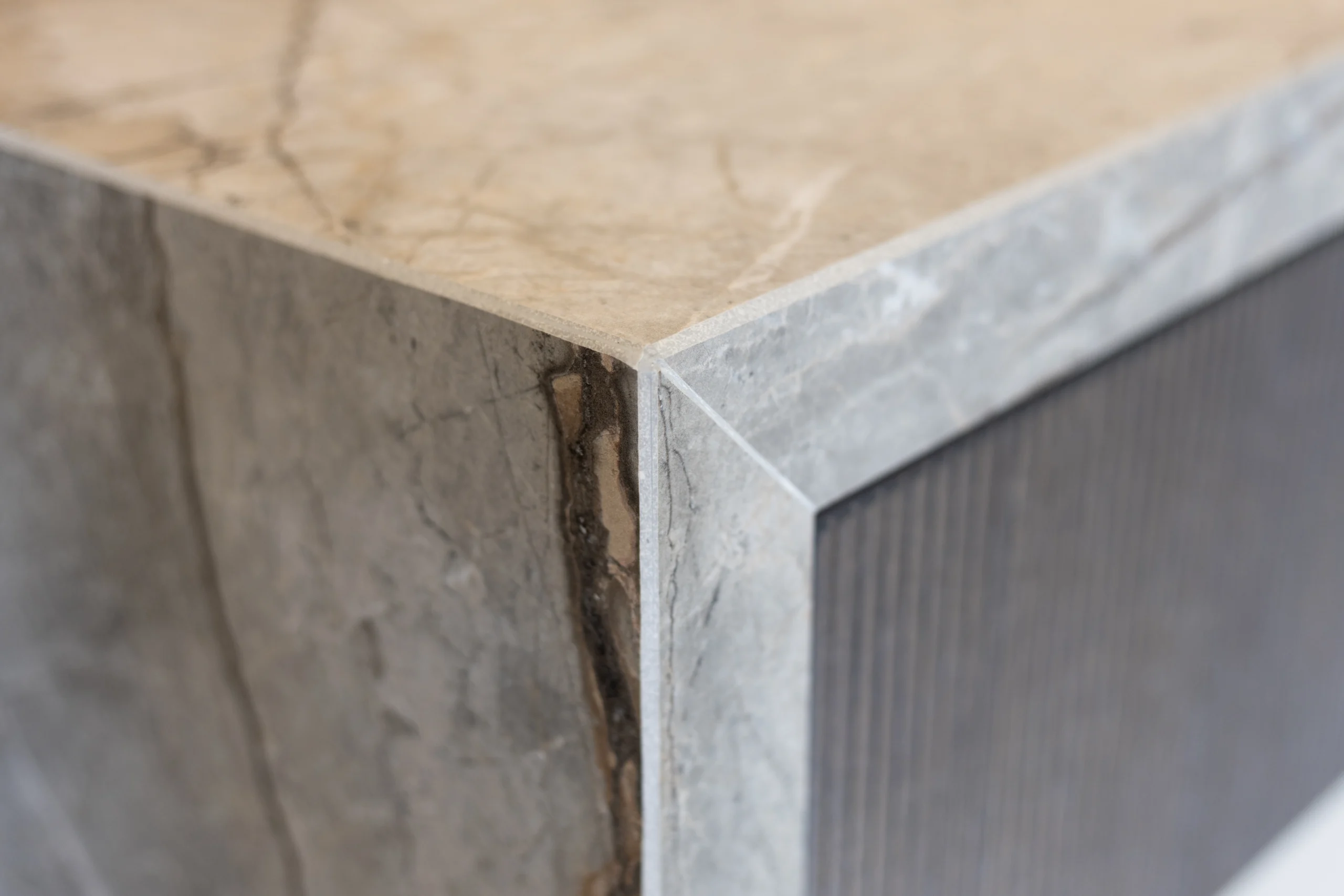 Close-up van een meubelhoek met lichte marmeren bovenkant en grijze, gepolijste zijkanten, scherp afgewerkt