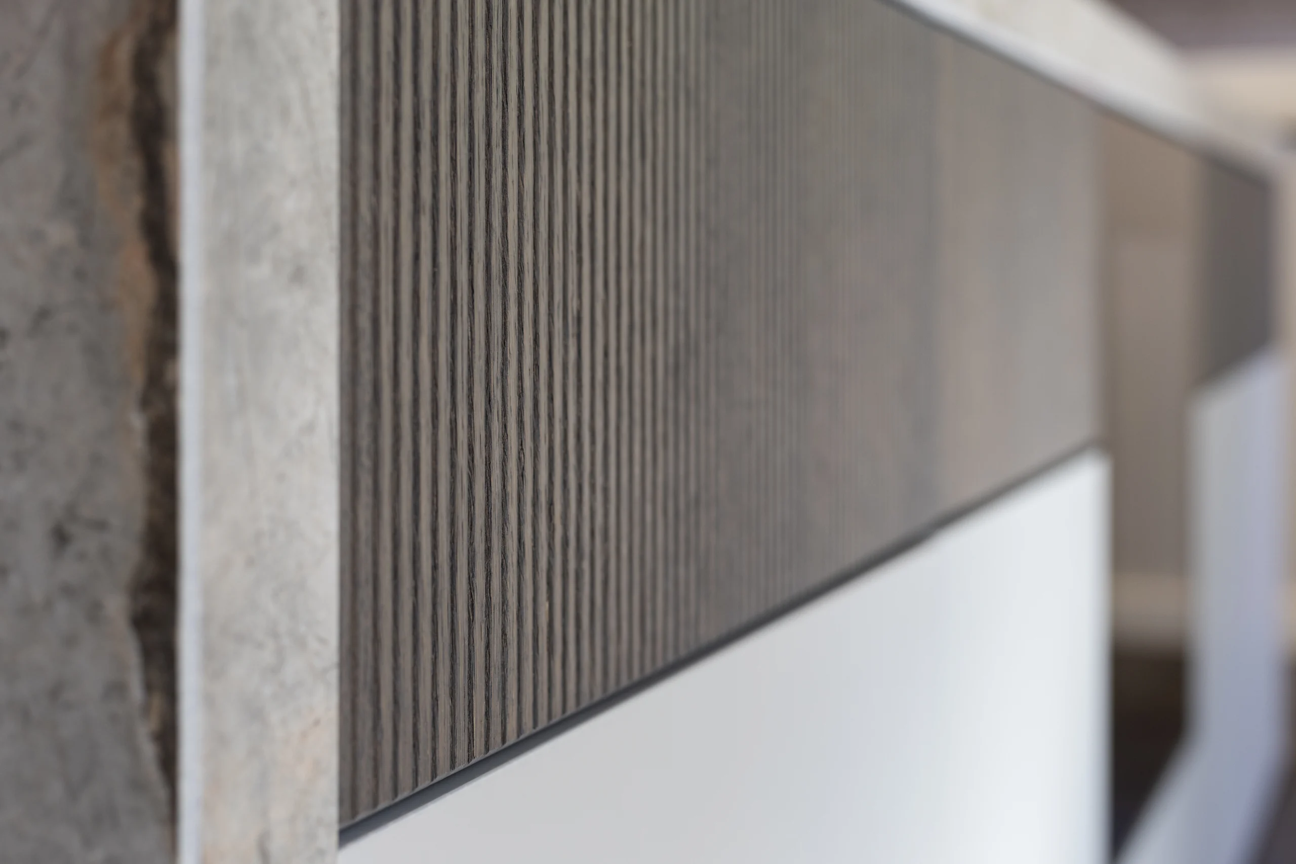 Close-up van een wand met verticale donkere houtstructuur, glad wit oppervlak en ruw beton