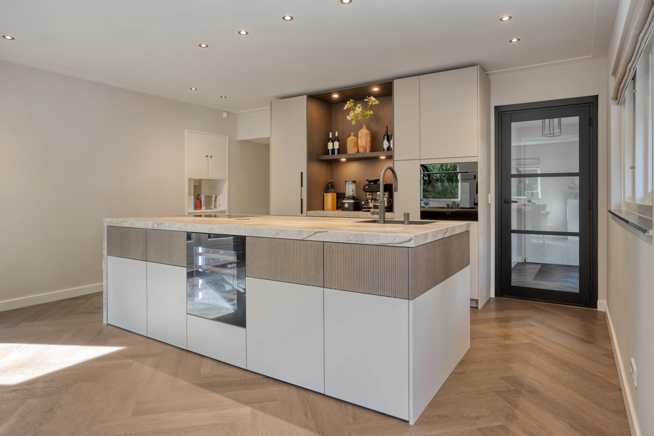 Moderne keuken met groot kookeiland, houten onderkasten, wand met keukenkastjes en glazen deur rechts