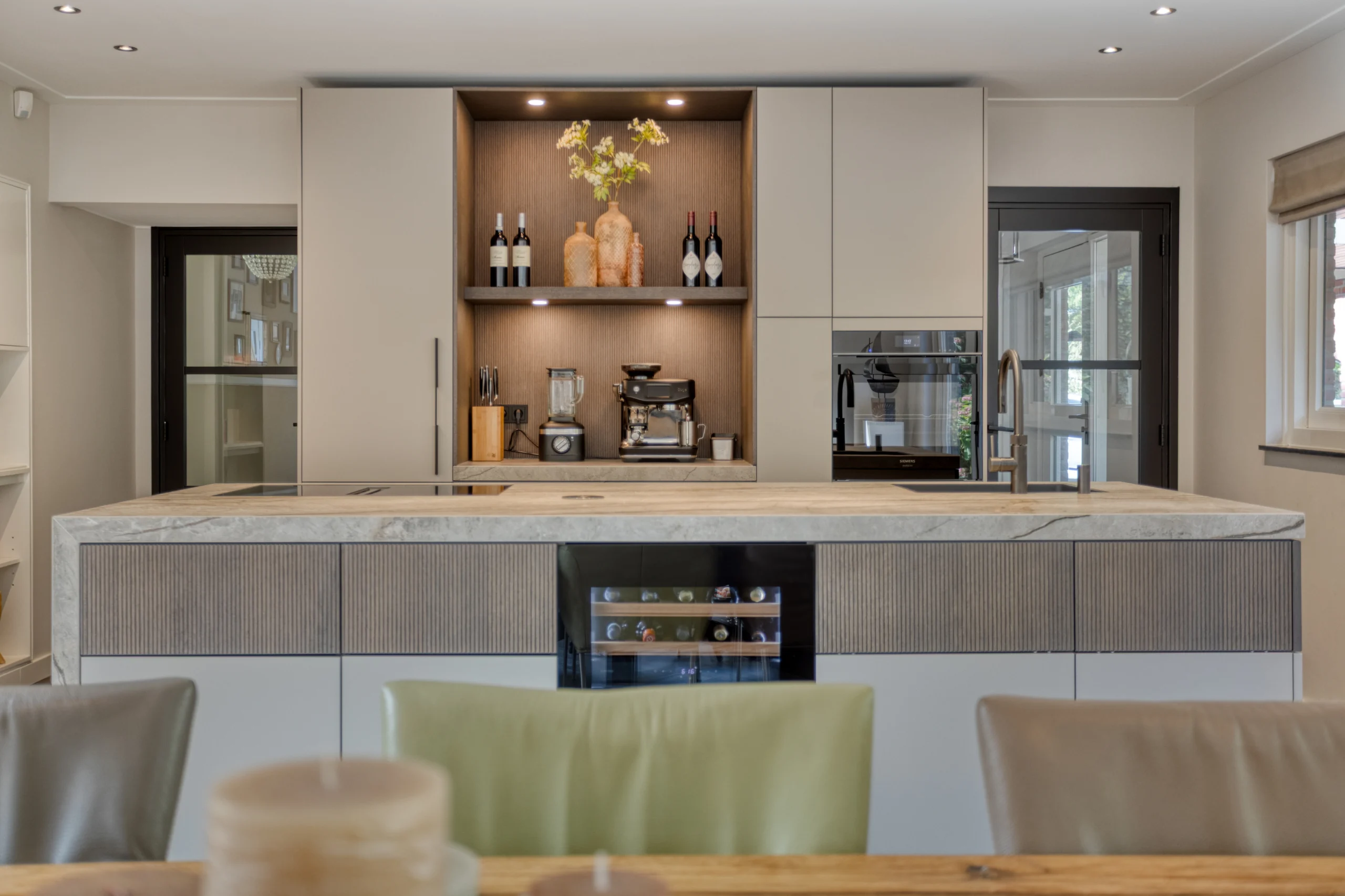 Moderne keuken met groot marmeren kookeiland, kasten, koffiezetapparaat en kleurrijke stoelen