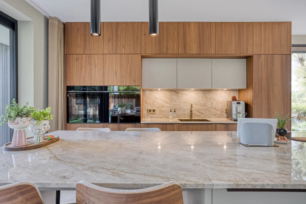 Moderne keuken met houten kasten, marmeren werkblad, eettafel en grote ramen met uitzicht