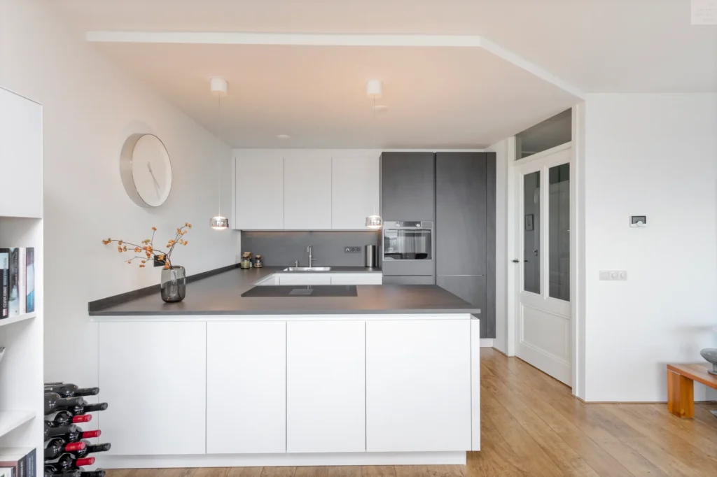 Moderne keuken met witte en antraciete kasten, hanglampen boven donkergrijs aanrechtblad en houten vloer